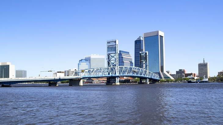 A city skyline and a bridge next to a river under a blue sky