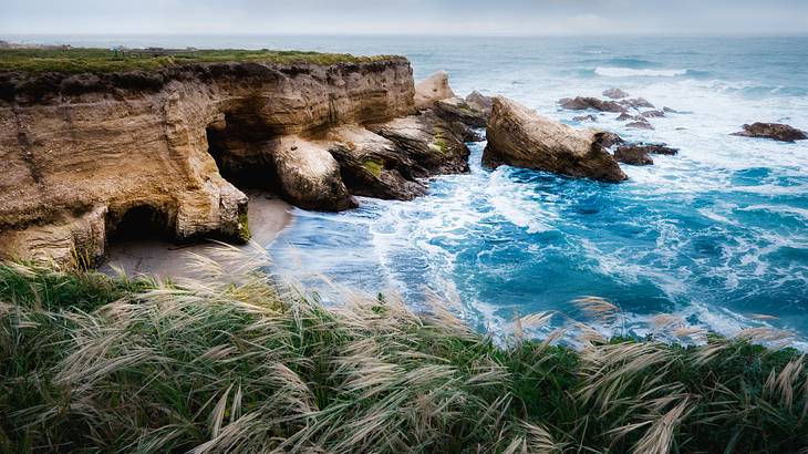 A grassy cliff overlooking a cove with the ocean water rushing to the shore