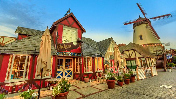 A cobbled street lined with old village shops, flower pots, and a windmill