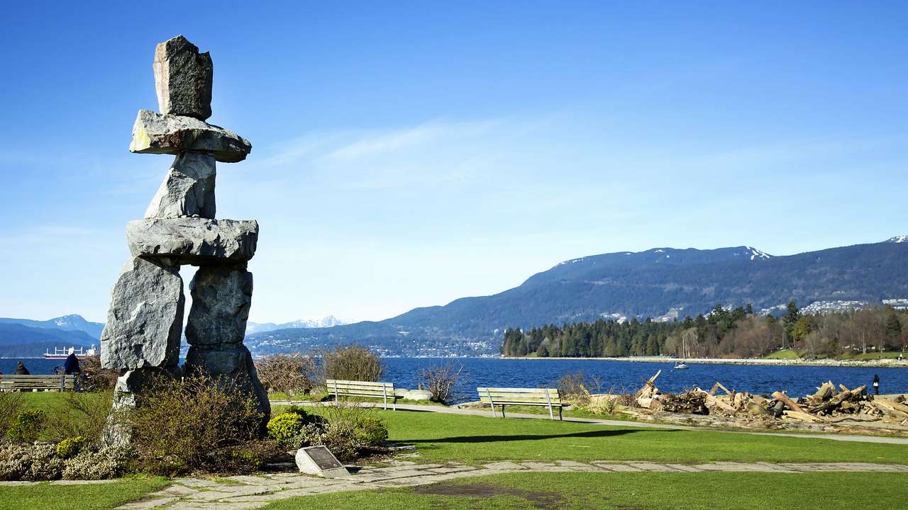 A rock sculpture on the grass next to the water with a mountain in the distance