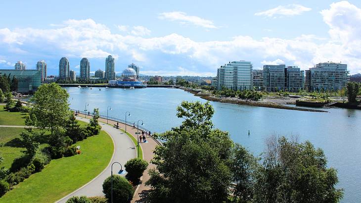 A creek with a park on one side and a cityscape on the other and a partly cloudy sky