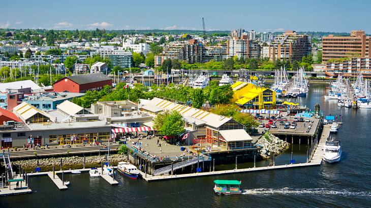 A waterfront full of buildings and people with a pier leading to boats on the creek