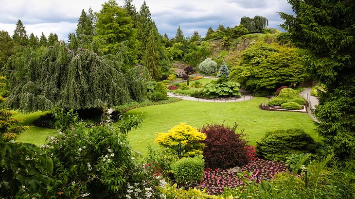 A park with green grass, colorful plants, trees, and walkways on a nice day