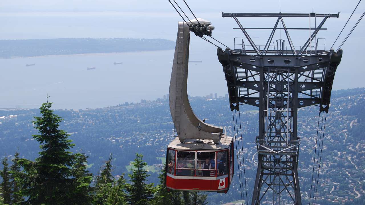 A cable car full of people and the tower supporting it with a view of the city below