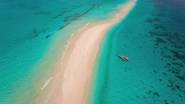 Aerial view of a sandbank with a dhow sailboat on clear blue water