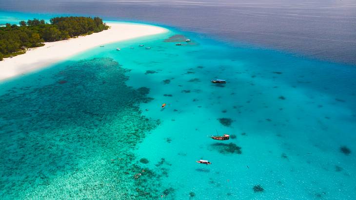 Aerial view of a lush, white-sand island with boats on clear blue water