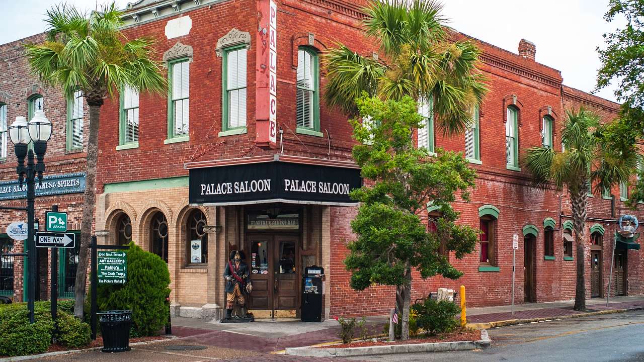 A red brick building with a "Palace Saloon" sign next to a street and palm trees