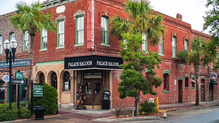 A red brick building with a "Palace Saloon" sign next to a street and palm trees