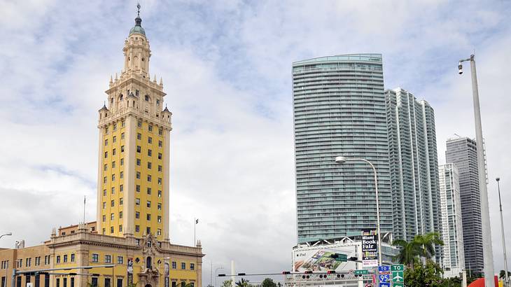 A Mediterranean Revival yellow tower by a glass building against a partly cloudy sky