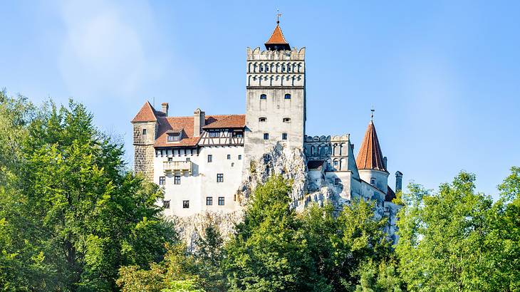 Romania vacation - A picture of a castle amongst trees during a sunny day, Romania