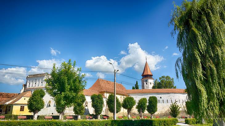 A view of a church, green trees and blue sky with clouds, Prejmer, Romania A view of a church, green trees and blue sky with clouds, Prejmer, Romania