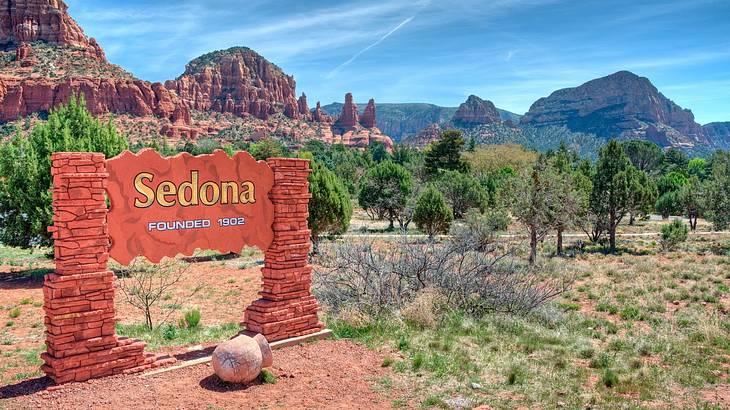 A sign that says "Sedona founded 1902" with trees and red rock cliffs behind it