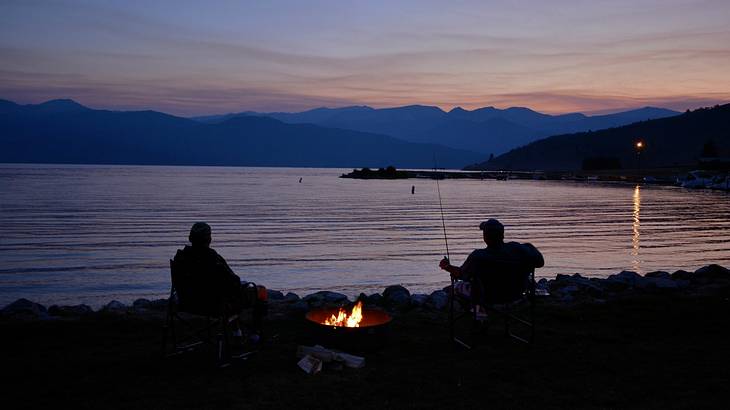 Silhouette of two people camping by calm water