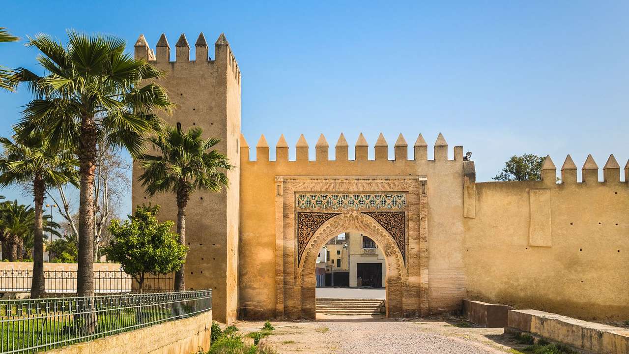 A fort-style structure next to a path and palm trees under a blue sky