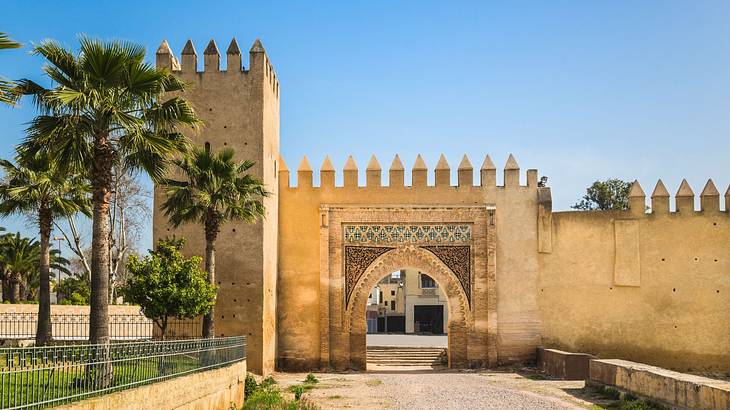 A fort-style structure next to a path and palm trees under a blue sky