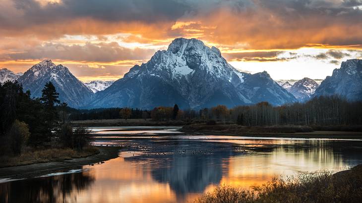 Body of water in front of the Teton Mountains with clouds above