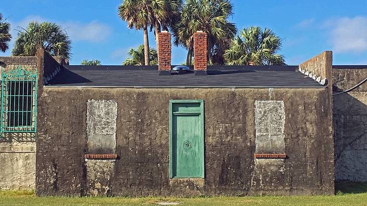 A small stone house with a green door and two chimneys next to palm trees