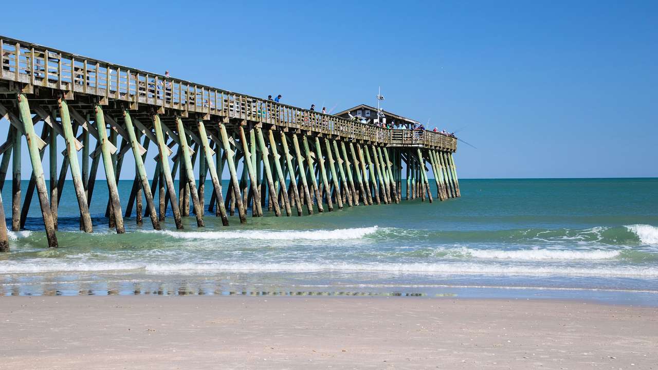 A long pier made of wood at the beach under a clear blue sky