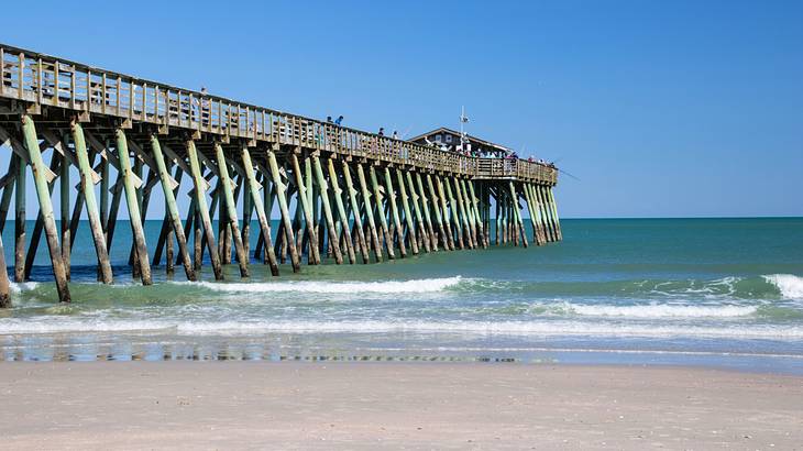 A long pier made of wood at the beach under a clear blue sky