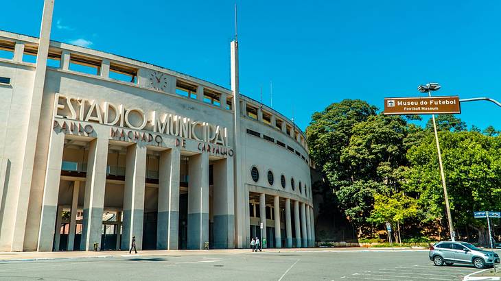 A round stone building next to trees and a street sign that says "Museu do Futebol"