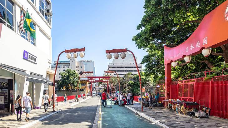 A red Japanese gate and streetlights along a street, next to buildings and trees