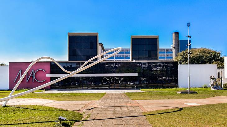 A modern glass building with a "MAC" sign, next to a path and green grass