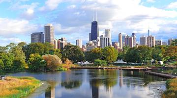 A lake with trees around it next to a city skyline under a cloudy sky