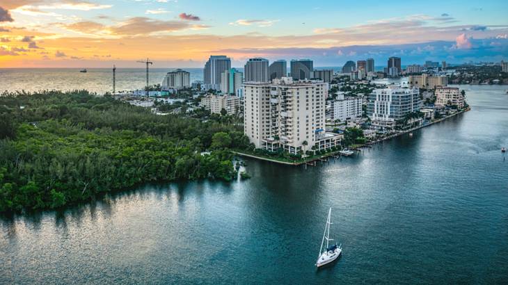 An aerial view of the water with a boat on it next to houses and trees at sunset