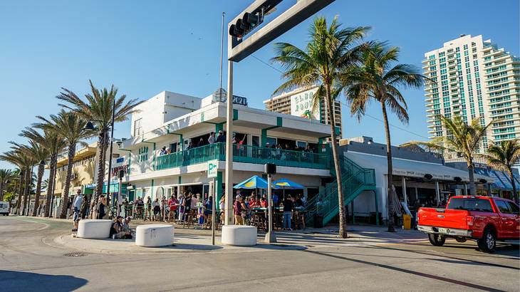 A beachy bar with two stories next to a road with palm trees on a clear day