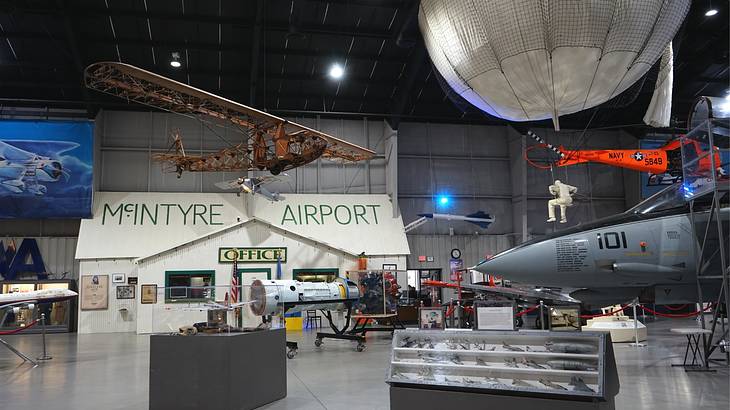 A museum exhibit with old airplanes and a small building that says "McIntyre Airport" A museum exhibit with old airplanes and a small building that says "McIntyre Airport"