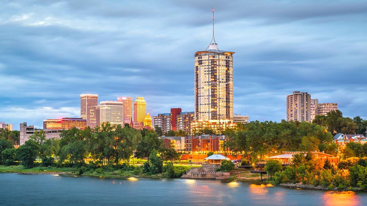 A river next to trees and illuminated buildings under a dark blue sky