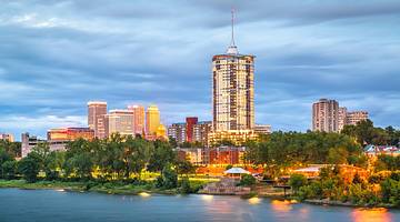 A river next to trees and illuminated buildings under a dark blue sky