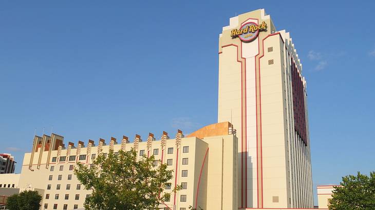 A hotel building with a "Hard Rock" logo next to trees and a blue sky A hotel building with a "Hard Rock" logo next to trees and a blue sky