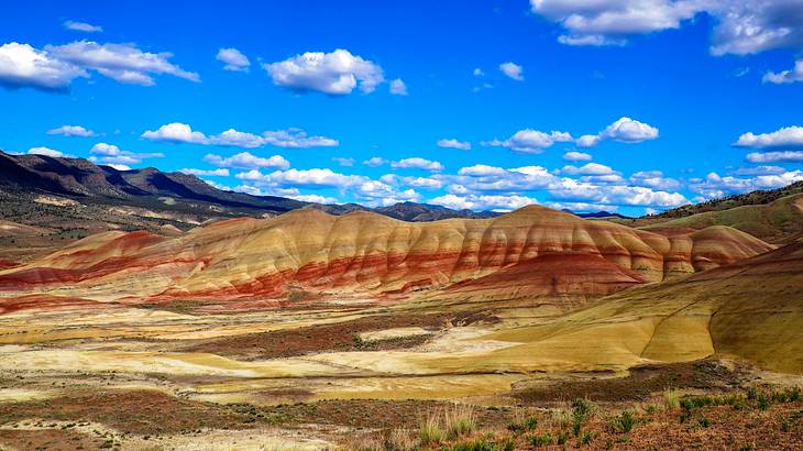 Barren hills with brown and red stripes against a partly cloudy sky