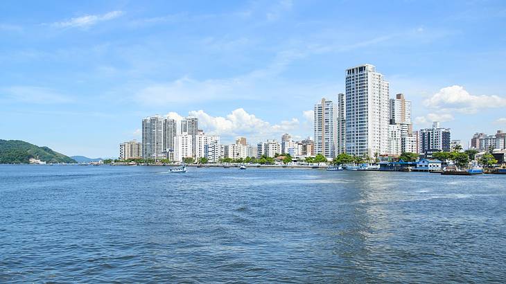 City buildings and a greenery-covered hill next to water under a blue sky