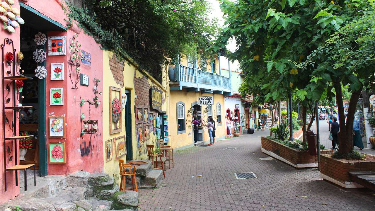 A brick street with trees on one side and pink and yellow buildings on the other