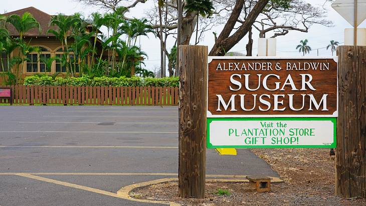 A wooden sign for the Sugar Museum and a house with a fence across the street