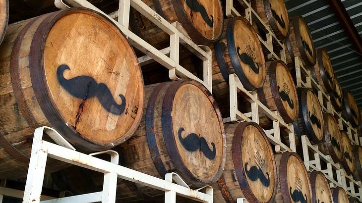 Rows of wooden casks on top of each other, each one with a mustache on its face