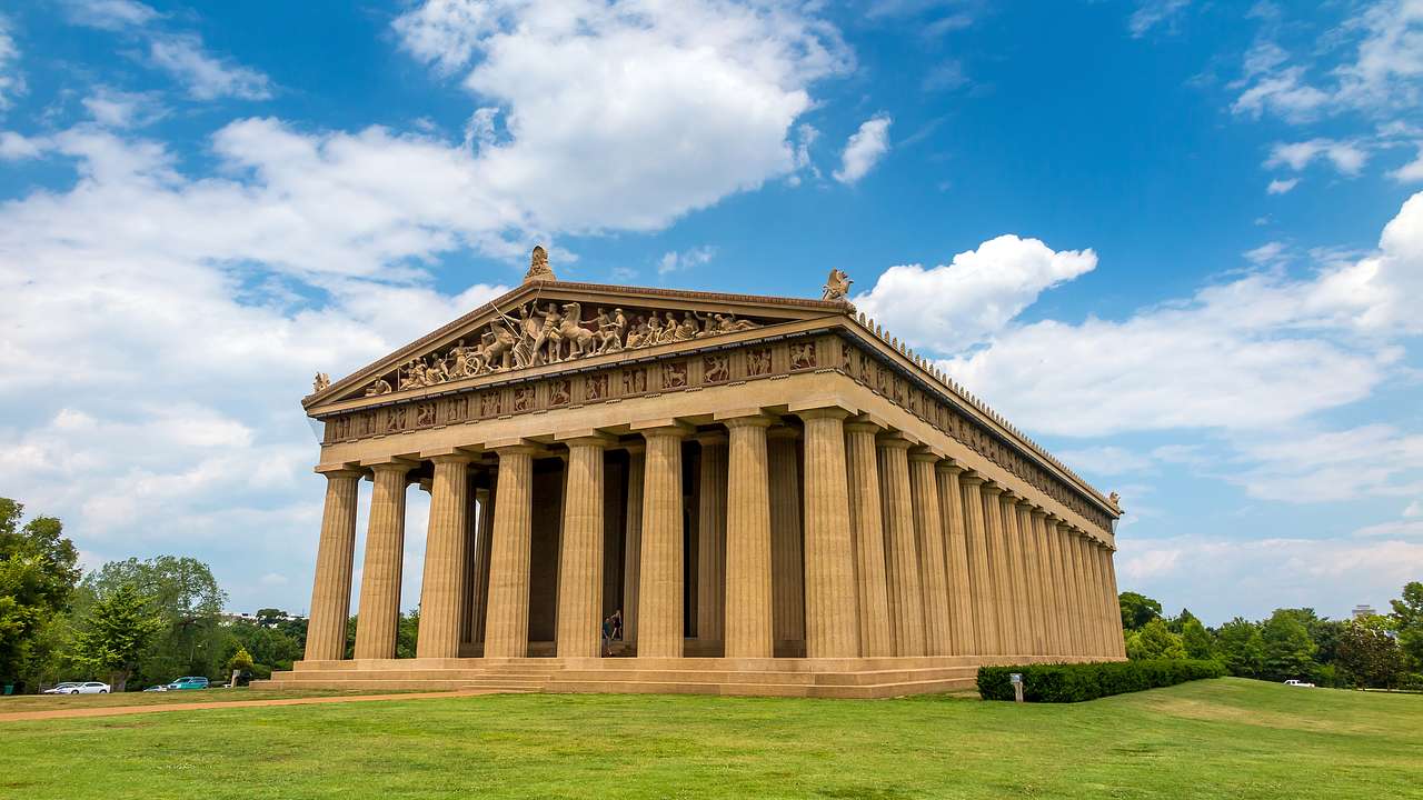 A Greek temple with carvings of a battle above the columns, surrounded by green grass