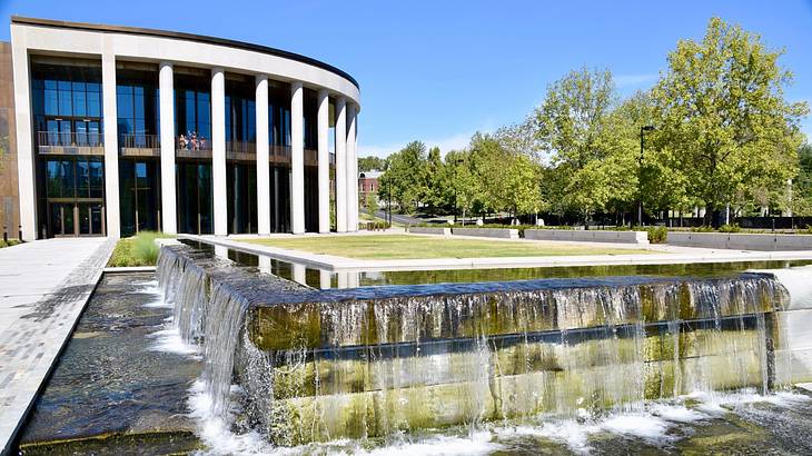 An artificial waterfall and a walkway in front of a round building with columns