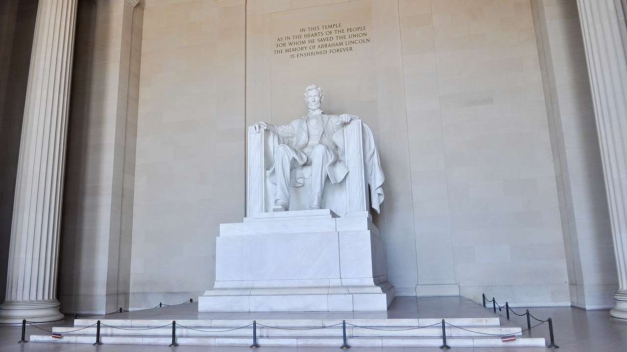 A white marble statue of a bearded man sitting on a throne with writing on the wall
