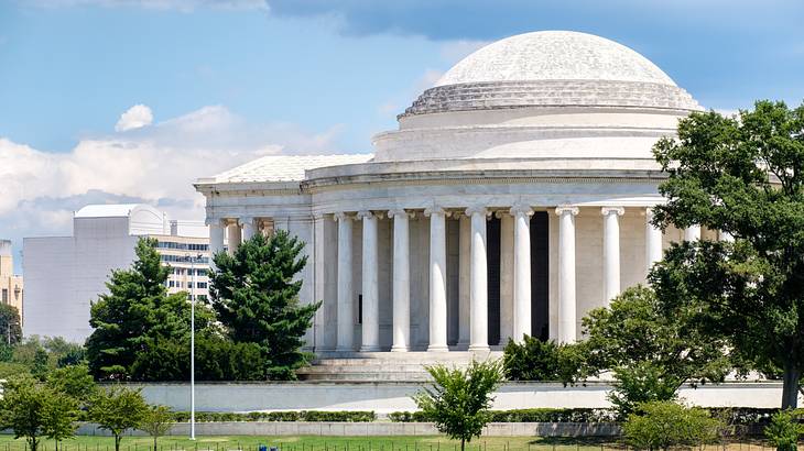 A large white building with many columns and a dome with trees and a front lawn