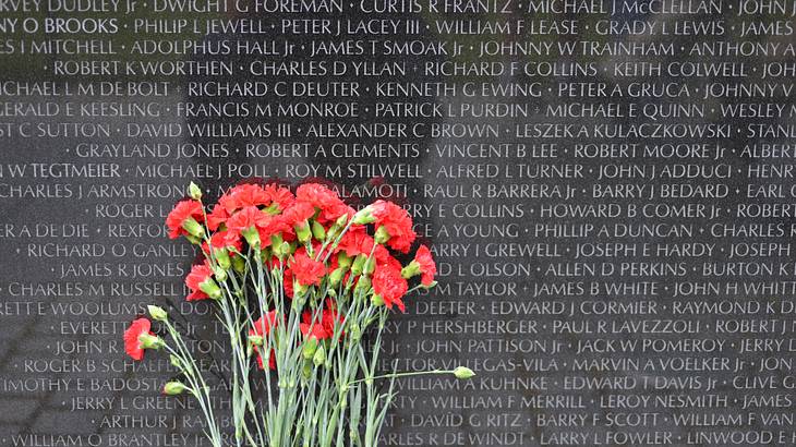 A black granite wall engraved with names next to a bunch of red flowers