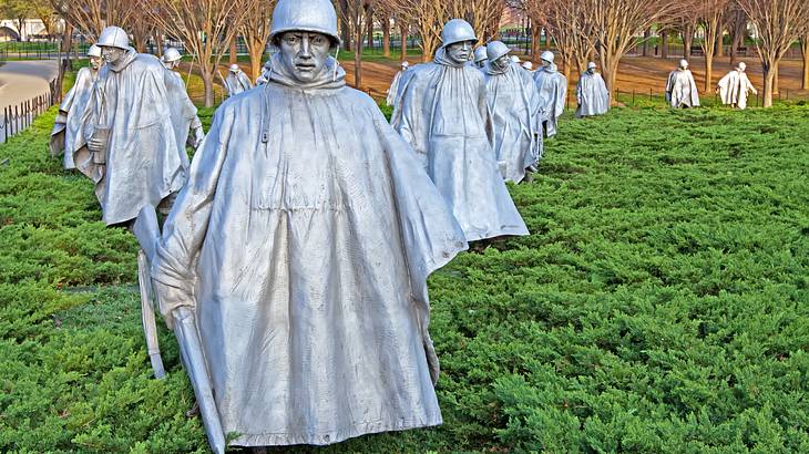 Stainless steel statues of soldiers in a field of bushes with trees in the back
