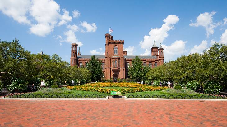 A red sandstone castle next to green grass, trees, and a brick path