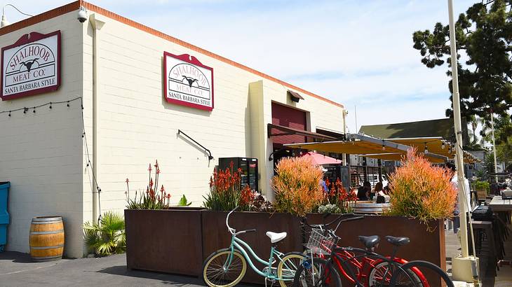 A white square building with outdoor dining, tall plant boxes, and bikes lined up