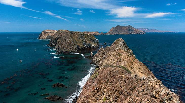 A chain of small rocky islands in the blue sea underneath a partly cloudy sky