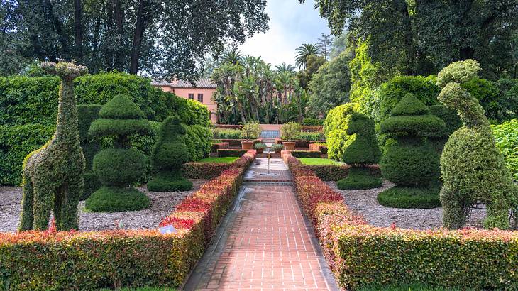 Plant sculptures of animals next to hedges with a brick path in the middle