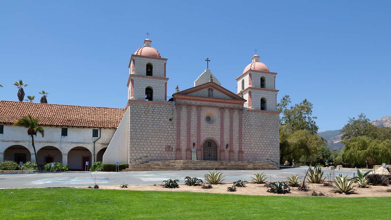 An old church with two bell towers and a lawn with some plants next to it