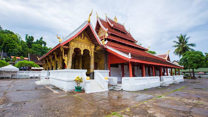 A temple with a red roof, golden columns, intricate carvings, and white steps